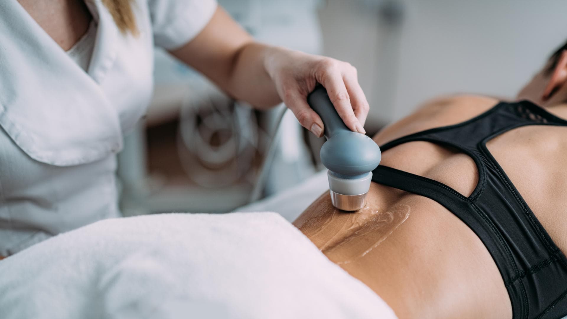Ultraschalltherapie kann bei Schmerzen und Reizungen helfen. Physiotherapeutin behandelt den Rücken einer Patientin mit einem Ultraschallgerät.