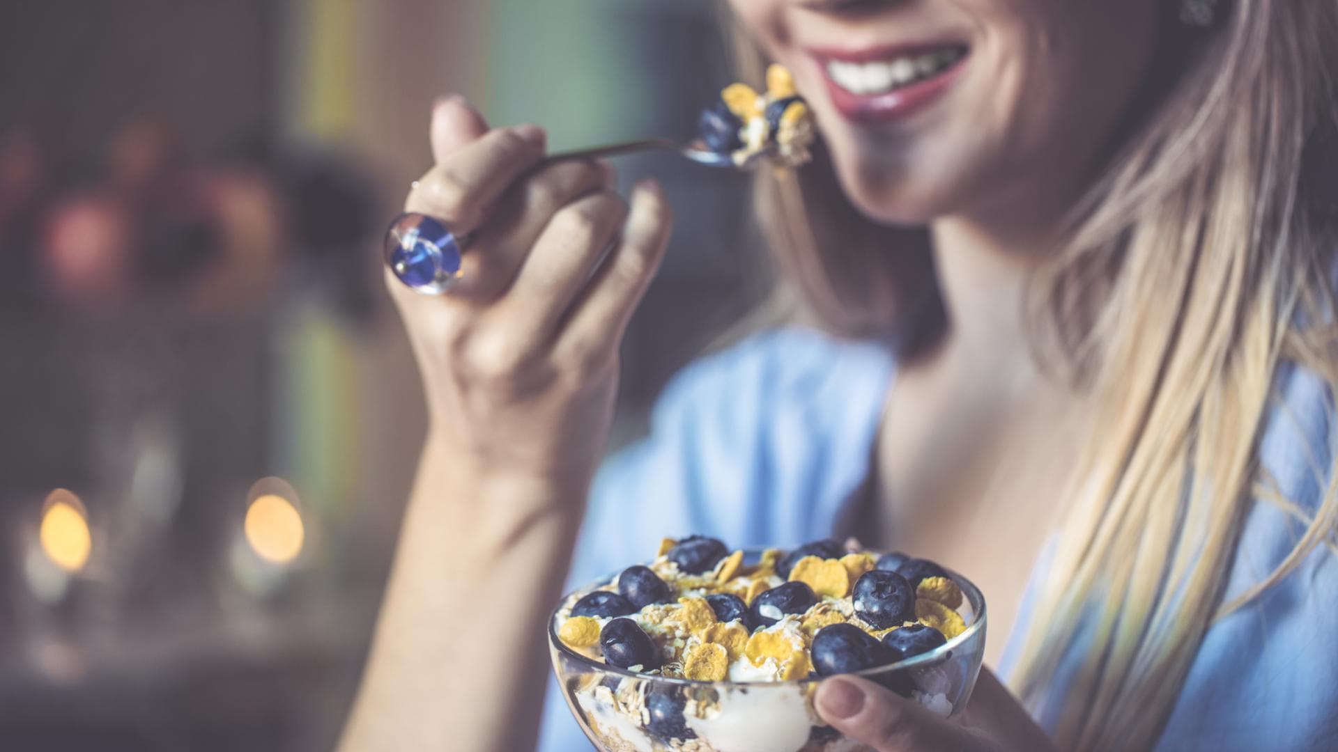 Welche Lebensmittel sind gut für die Zähne? Frau mit schönen Zähnen isst einen Löffel Müsli mit Joghurt