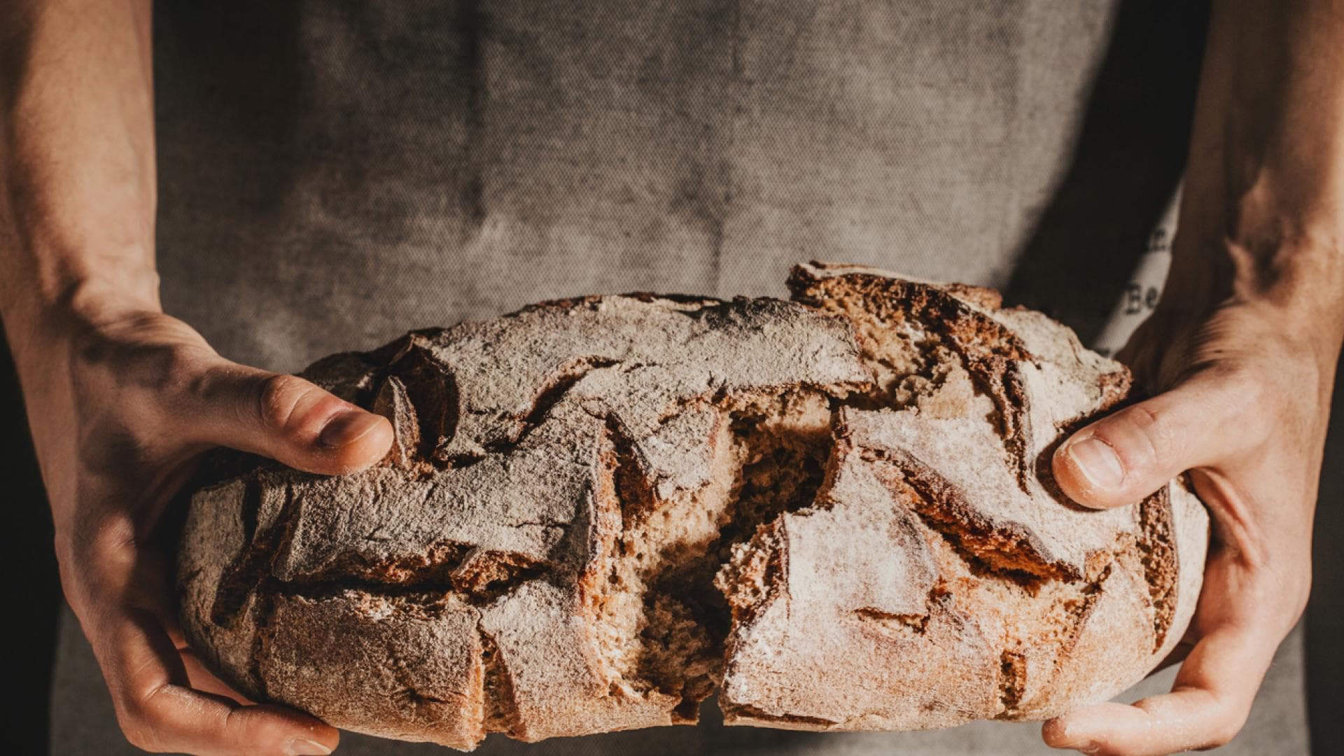 Knuspriges Brot gelingt mit diesen Tipps immer. Mann bricht ein frischgebackenes Brot durch