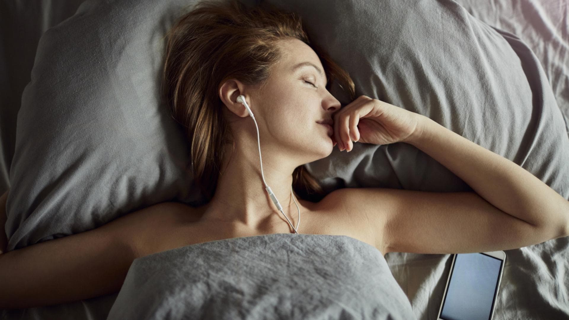 Frau liegt im Bett und hört Hörbücher zum Einschlafen Frau liegt im Bett und hört Hörbücher zum Einschlafen