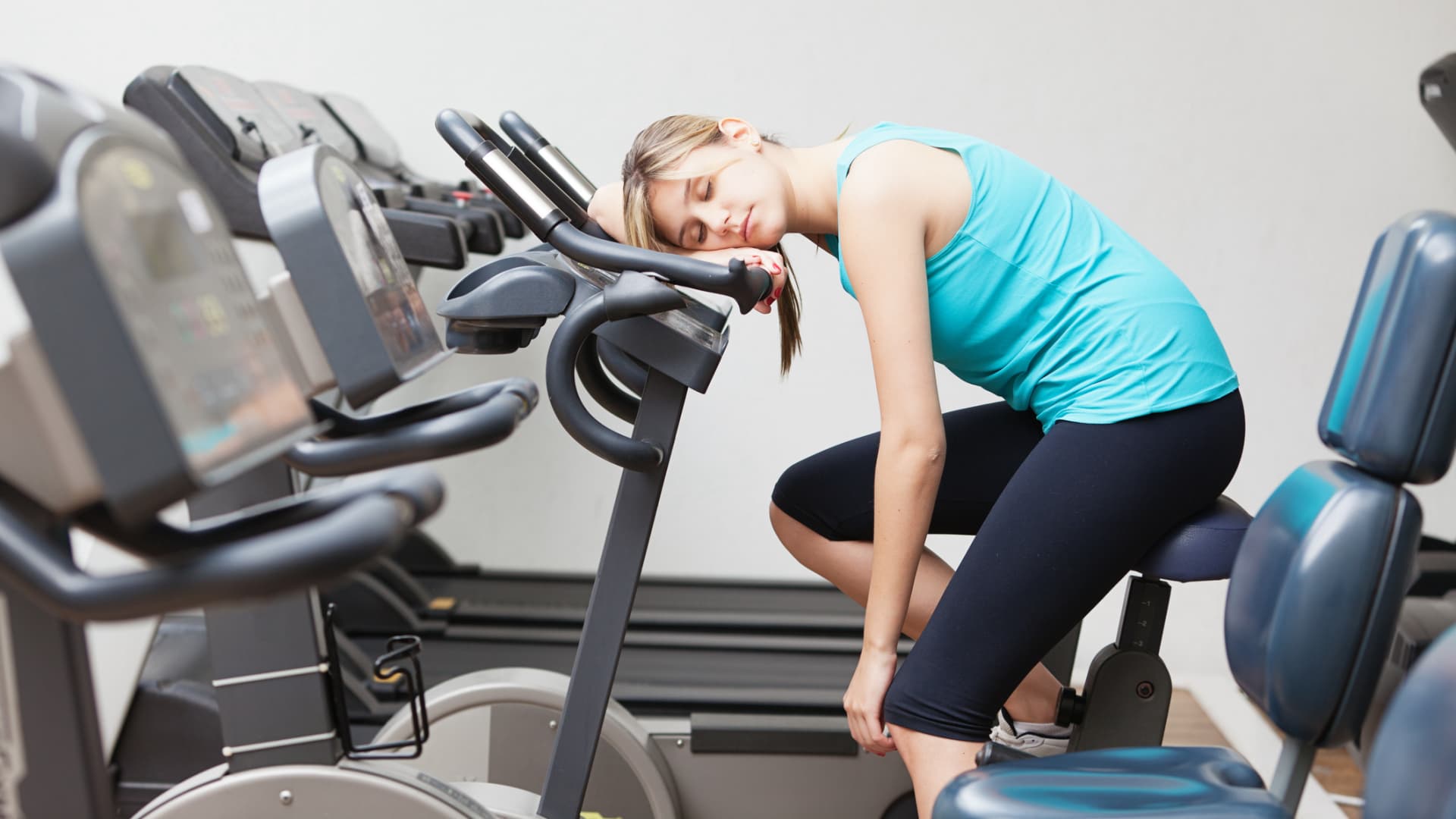 Motivationssprüche für den Sport können uns, wenn der innere Schweinehund mal wieder besonders stark ist. Frau sitzt müde auf einem Hometrainer