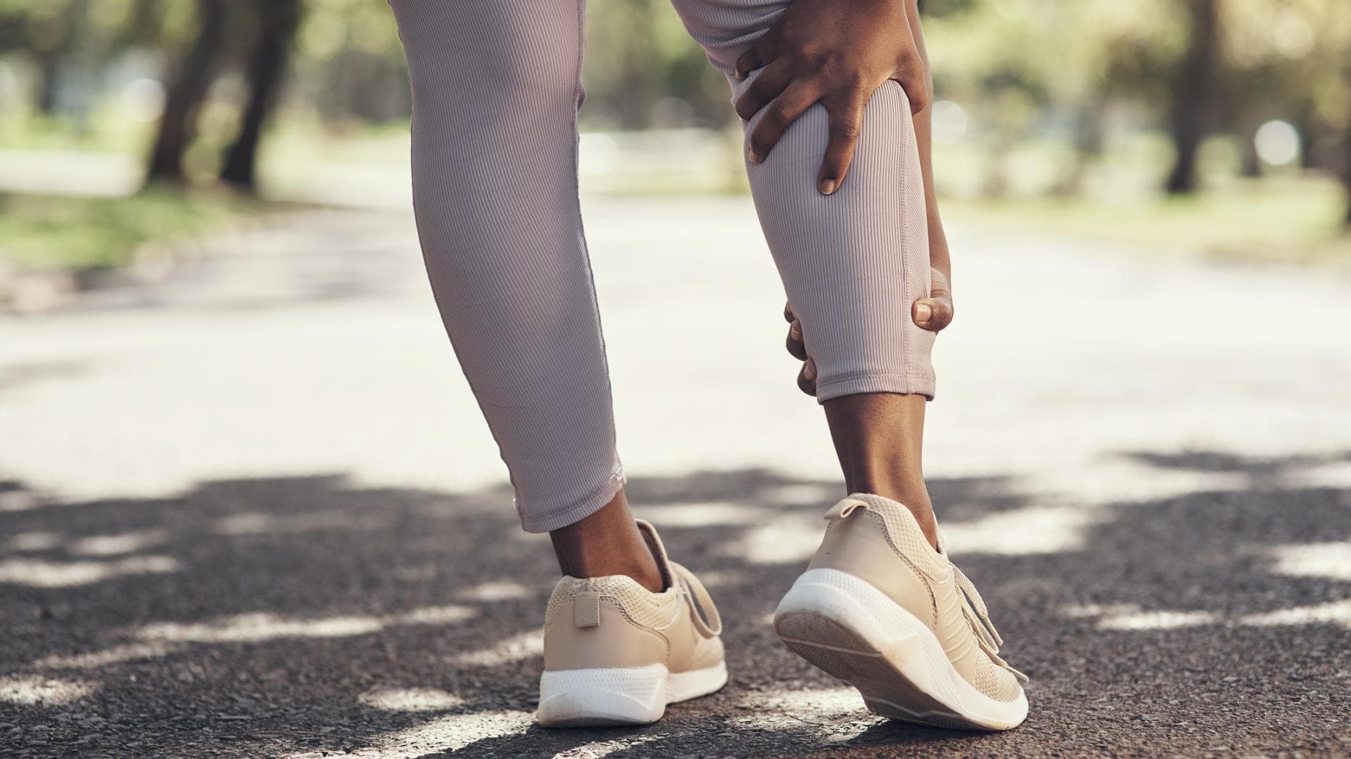 Eine Joggerin hält sich die schmerzende Wade