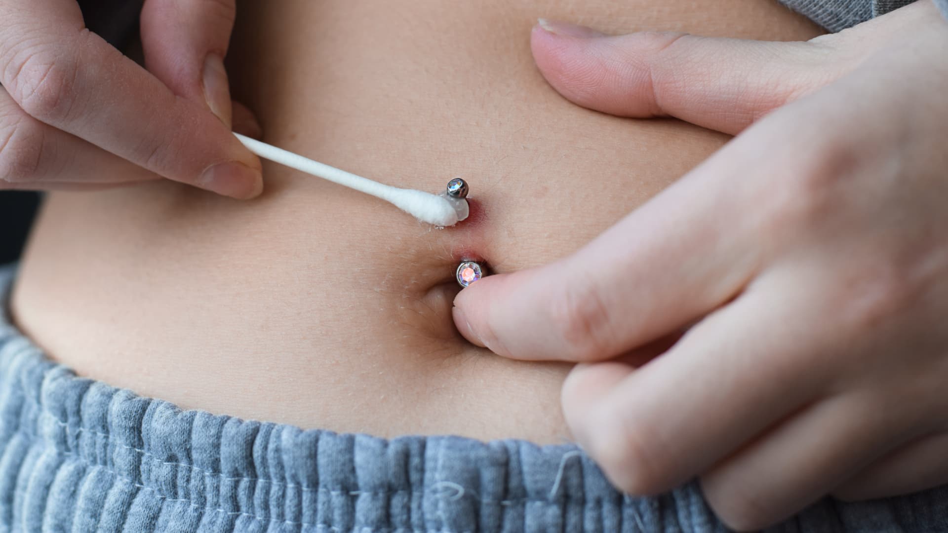 Um Komplikationen zu vermeiden, ist die richtige Piercing-Pflege von entscheidender Bedeutung. Frau pflegt ihr Bauchnabel-Piercing