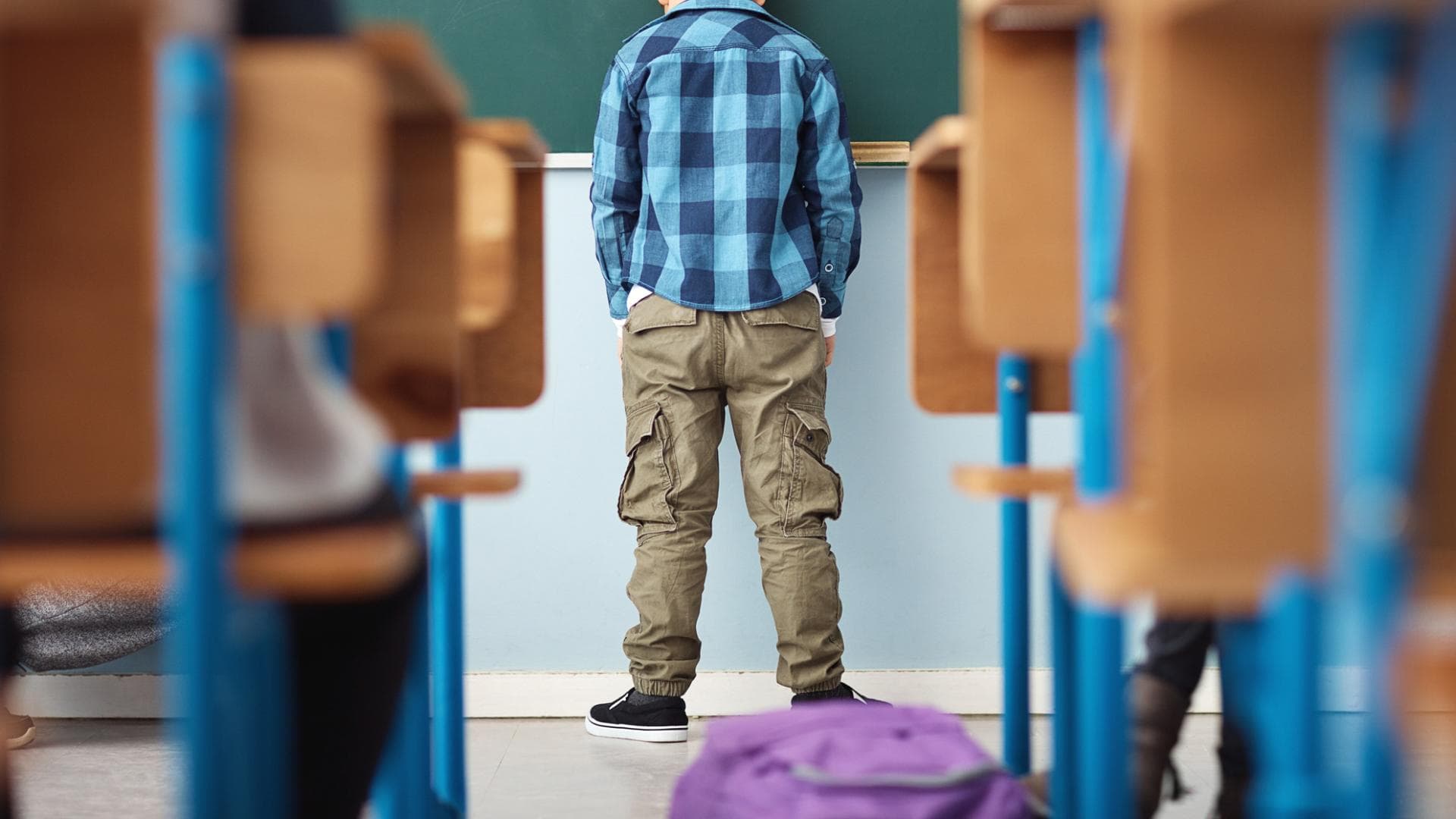Schulstress kann krank machen rothaariger Schuljunge steht enttäuscht vor der Tafel mit Händen in den Taschen
