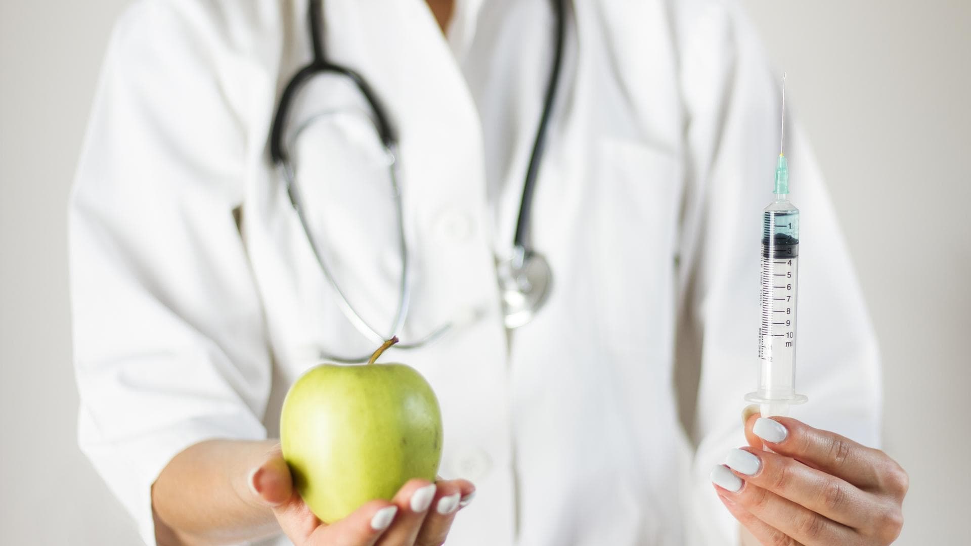 Ärztin hält Apfel in der einen und Spritze in der anderen Hand Ärztin hält Apfel in der einen und Spritze in der anderen Hand