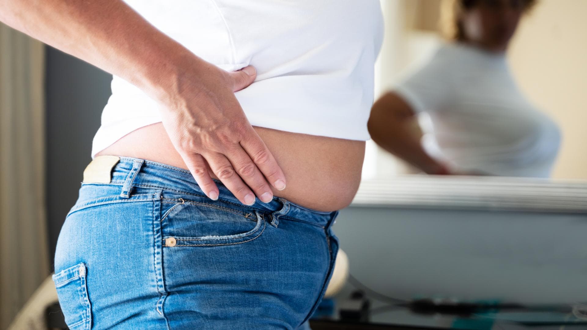 Frau guckt sich ihren Bauch im Spiegel an