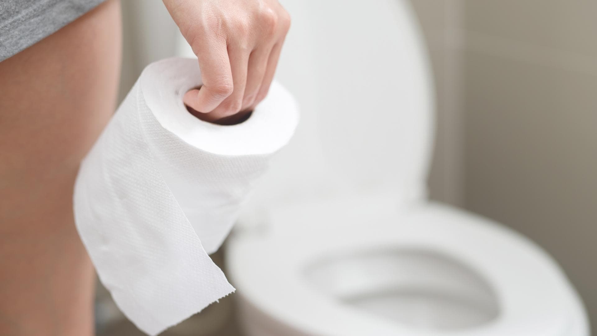 Frau steht mit Toilettenpapier in der Hand vor der Toilette Frau steht mit Toilettenpapier in der Hand vor der Toilette