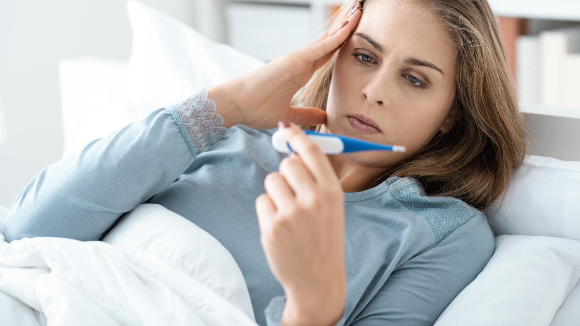 Frau schaut auf Fieberthermometer Frau schaut auf Fieberthermometer