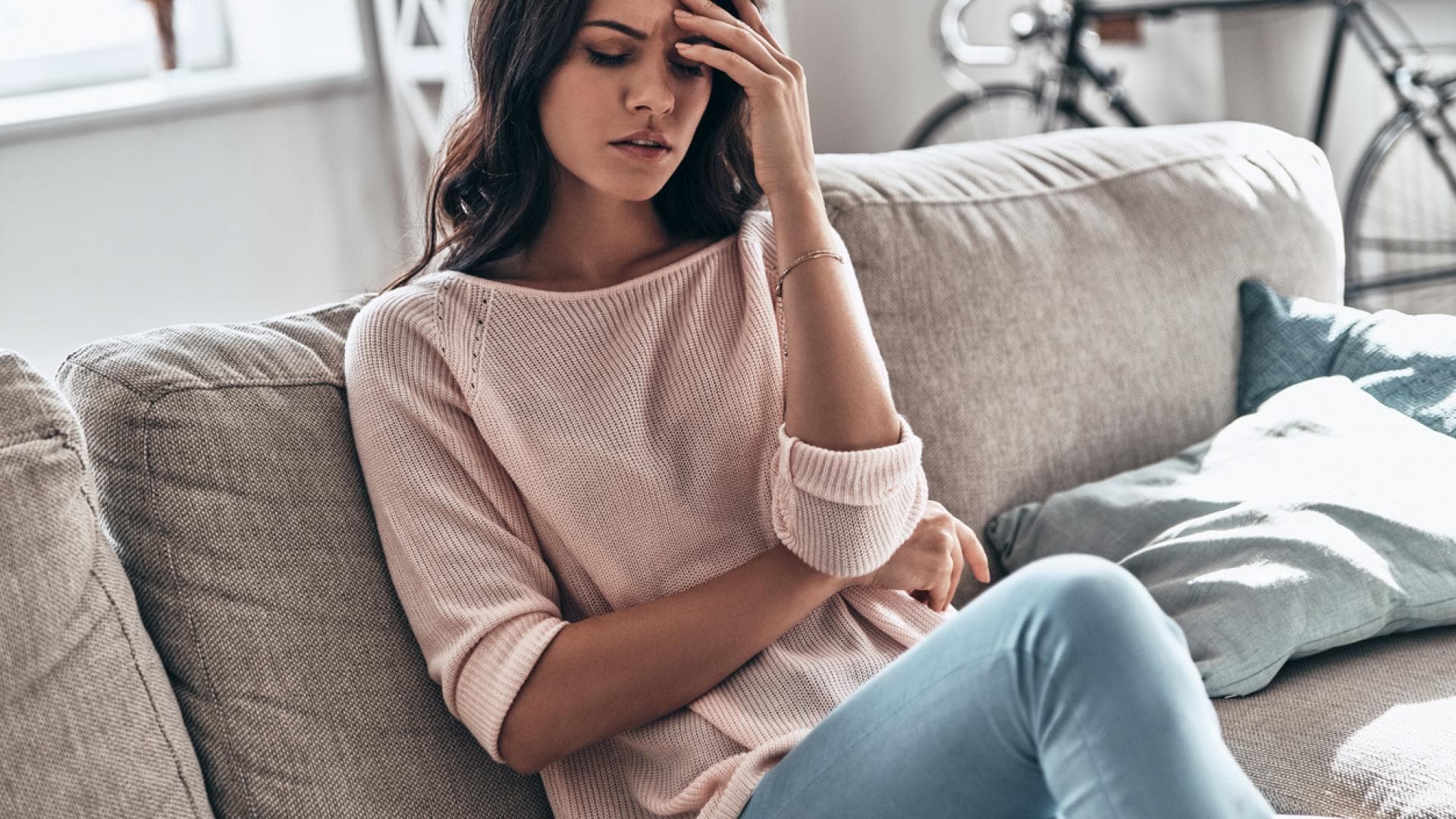Ein Symptom des Eiweißmangels ist körperliche Schwäche Frau hat einen Schwächeanfall und sitzt auf Sofa mit Hand an der Stirn