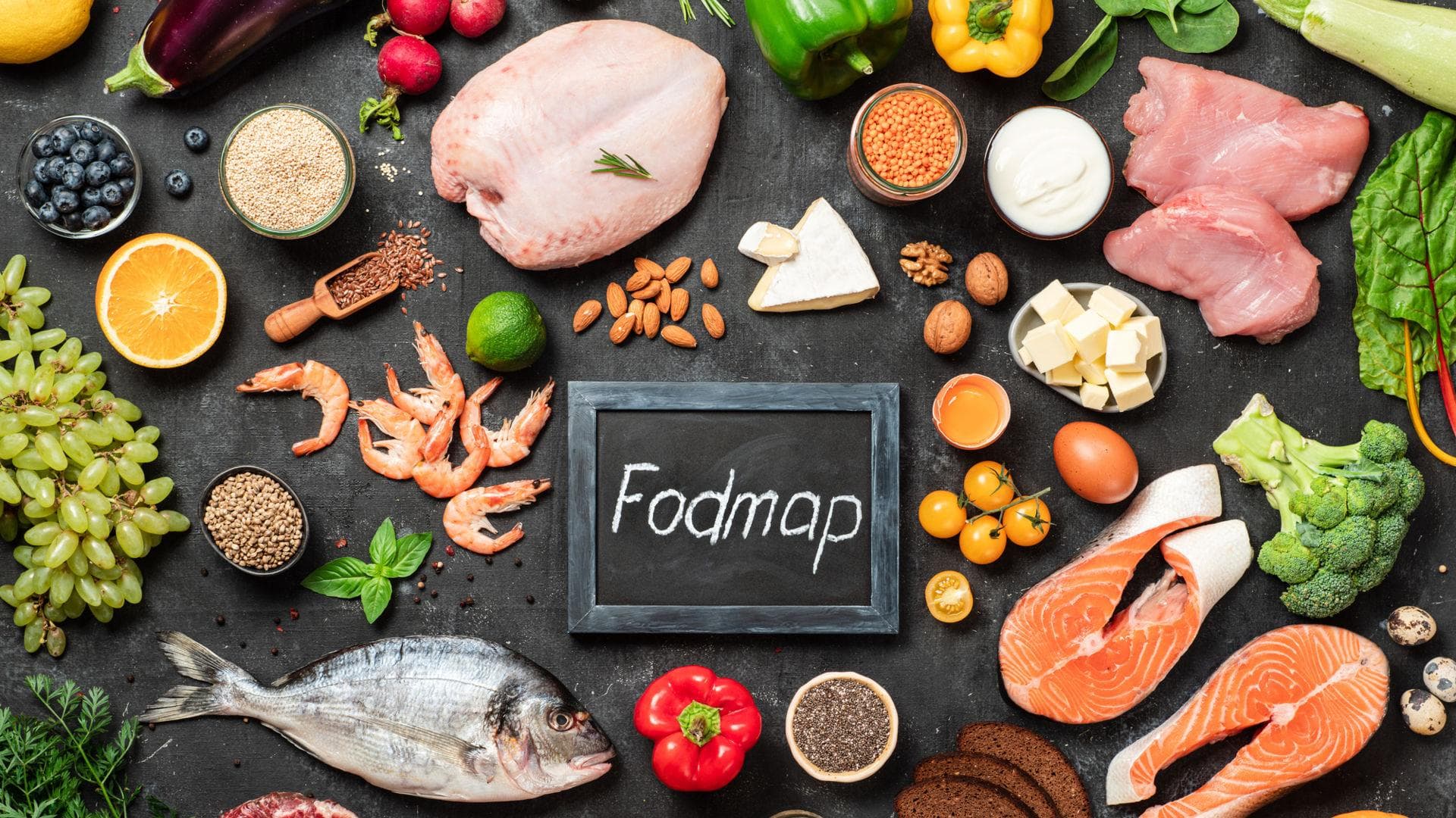 Bei Reizdarm sollten möglichst wenig FODMAPs gegessen werden. Lebensmittel der FODMAP-Diät auf schwarzer Schiefertafel arrangiert