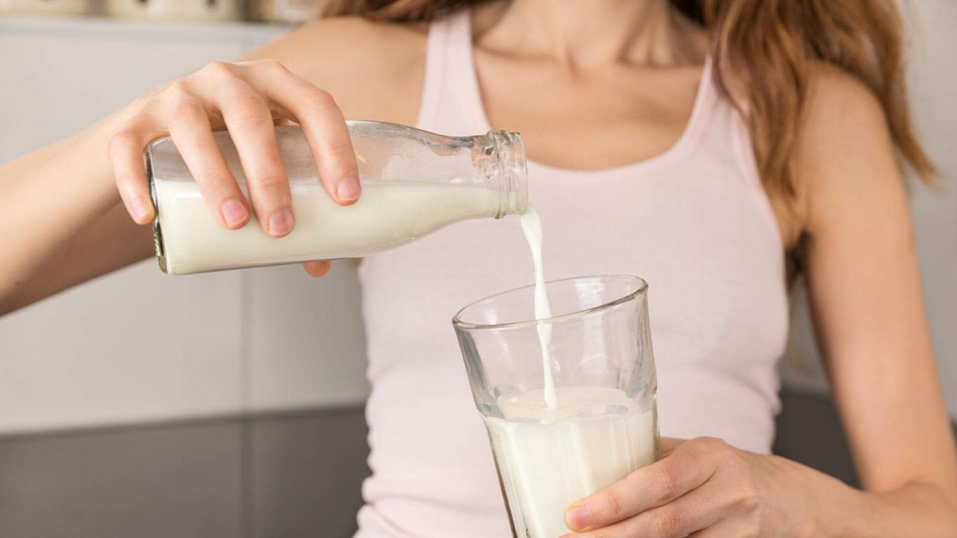 Frau gießt sich Milch in ein Glas ein