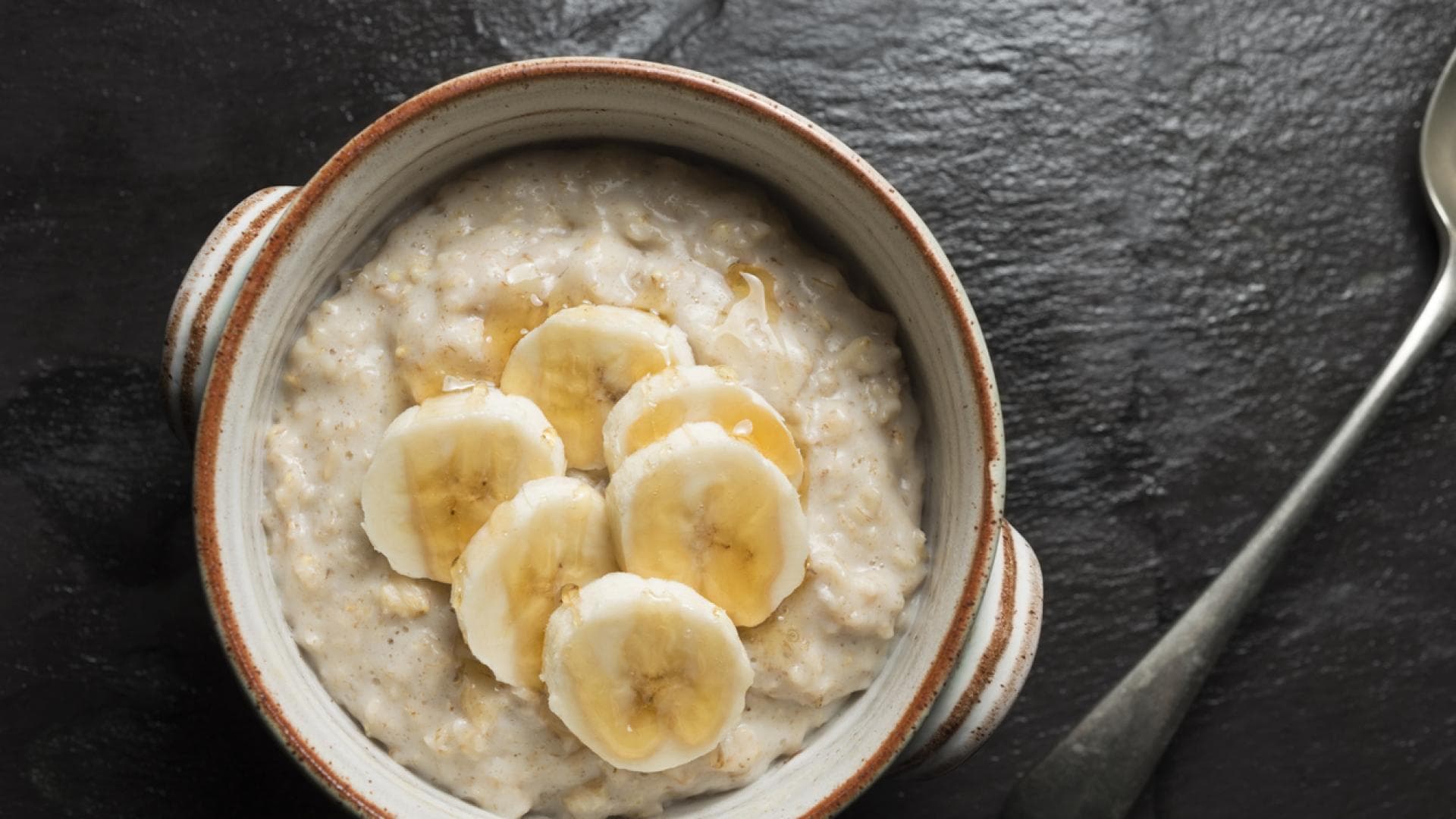 Bei Magen-Darm-Grippe essen wir am besten Schonkost Draufsicht einer Schüssel Porridge mit Bananenscheiben und Honig