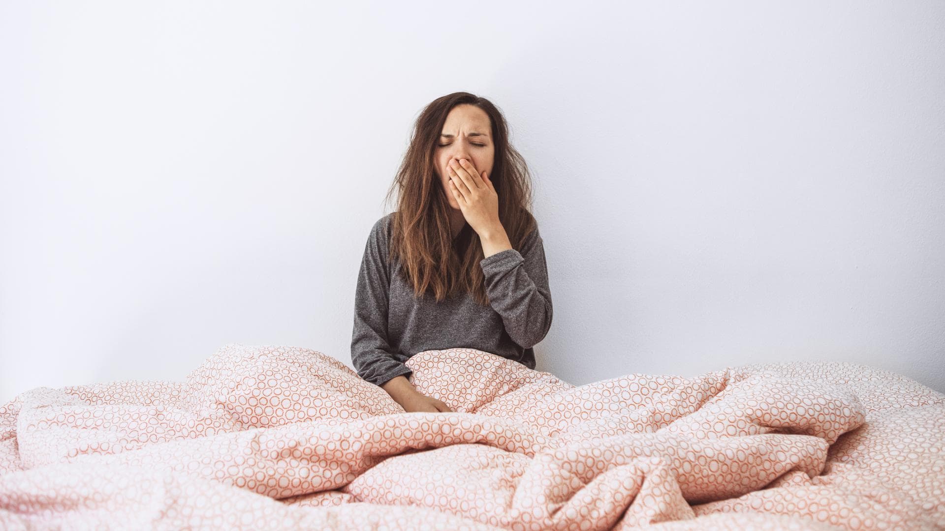 Frau sitzt im Bett und gähnt Frau sitzt im Bett und gähnt