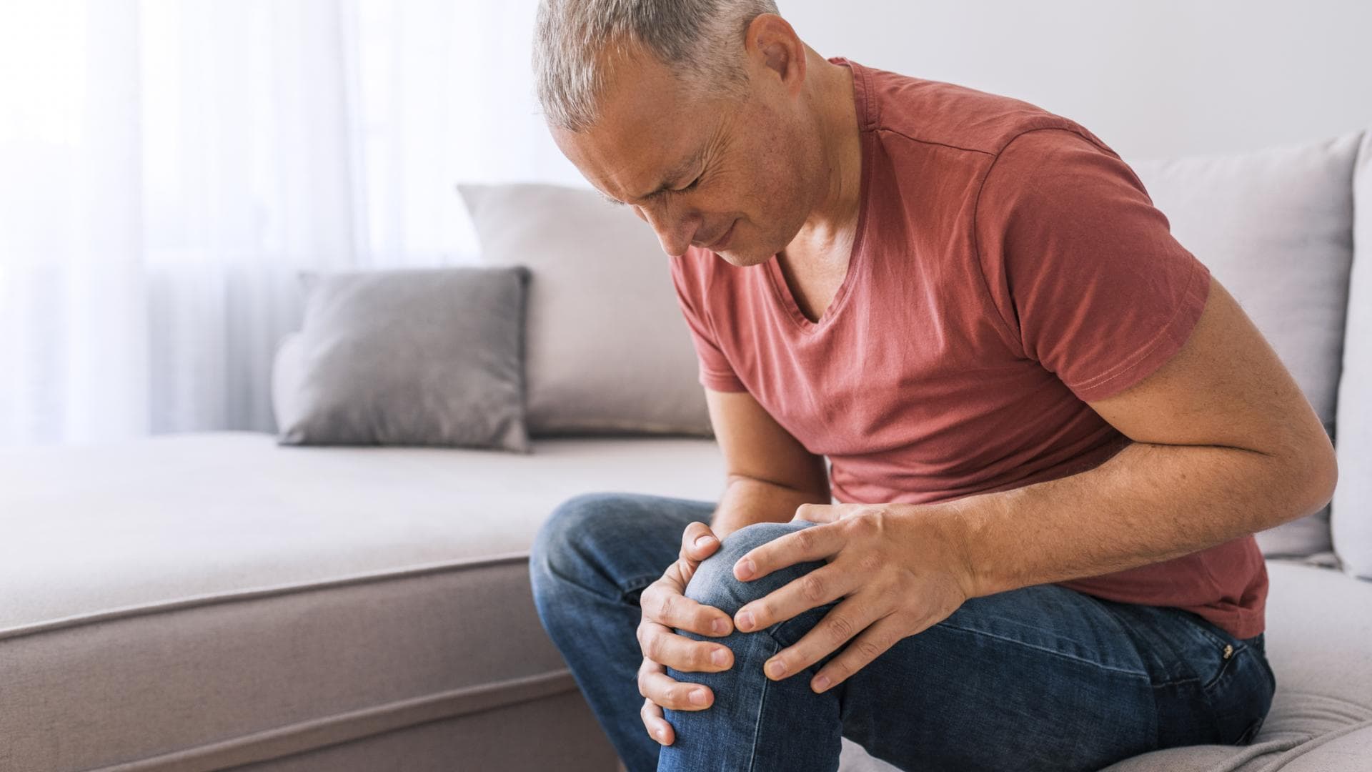 Ein Mann hält sich vor Schmerzen wegen einer Gelenkerkrankung das Knie. Ein Mann hält sich vor Schmerzen wegen einer Gelenkerkrankung das Knie.