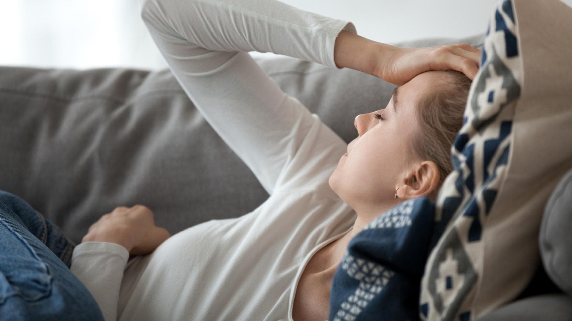Frau liegt mit Migräne aus dem Sofa Frau liegt mit Migräne auf dem Sofa