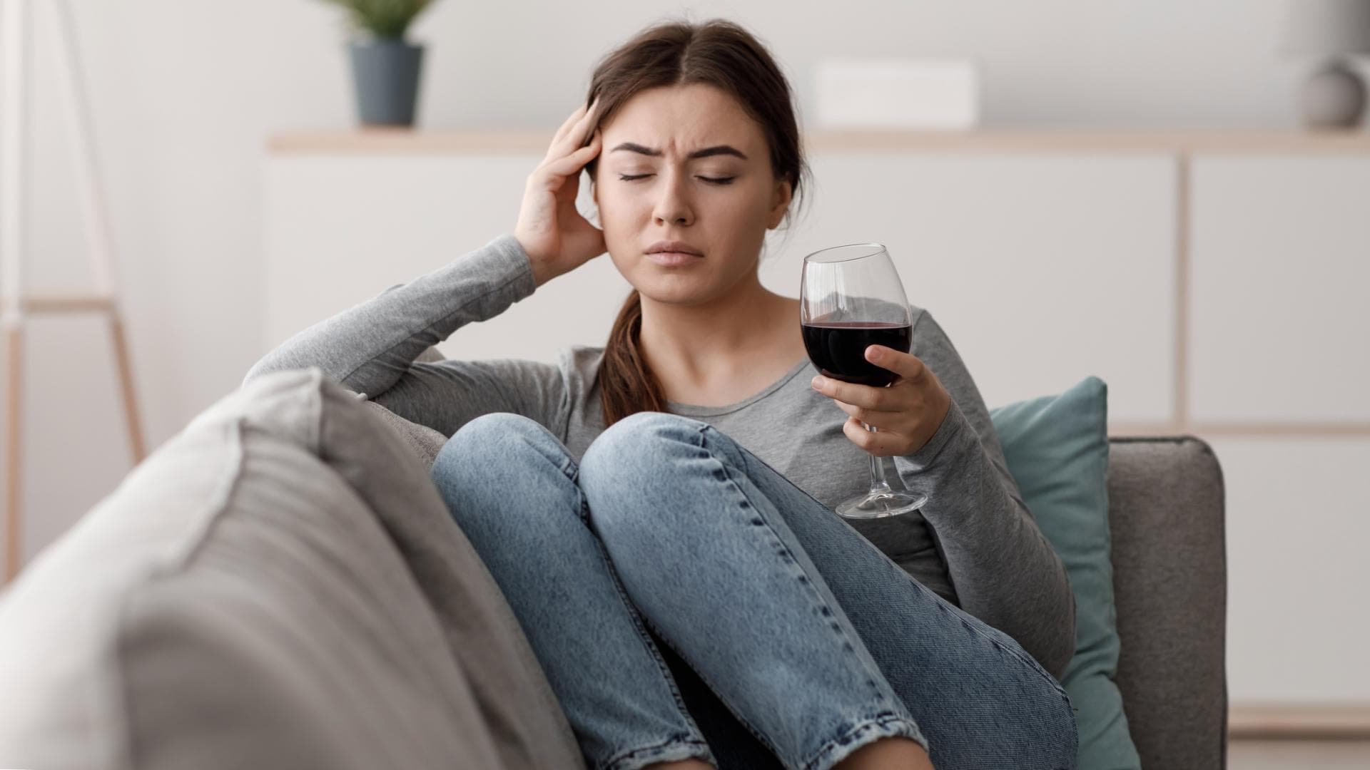 Frau sitzt mit einem Glas Wein in der Hand auf dem Sofa und fühlt sich unwohl