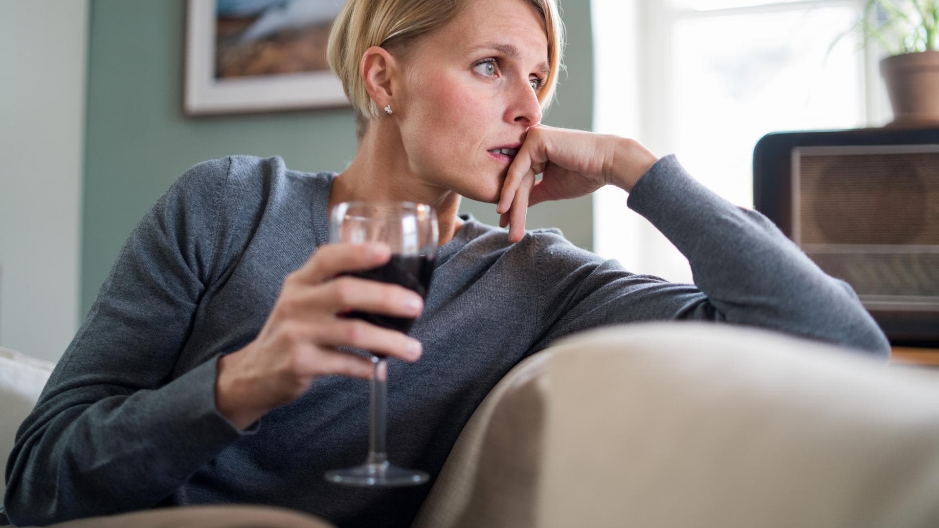 Nachdenkliche Frau sitzt auf dem Sofa mit einem Glas Wein in der Hand Nachdenkliche Frau sitzt auf dem Sofa mit einem Glas Wein in der Hand