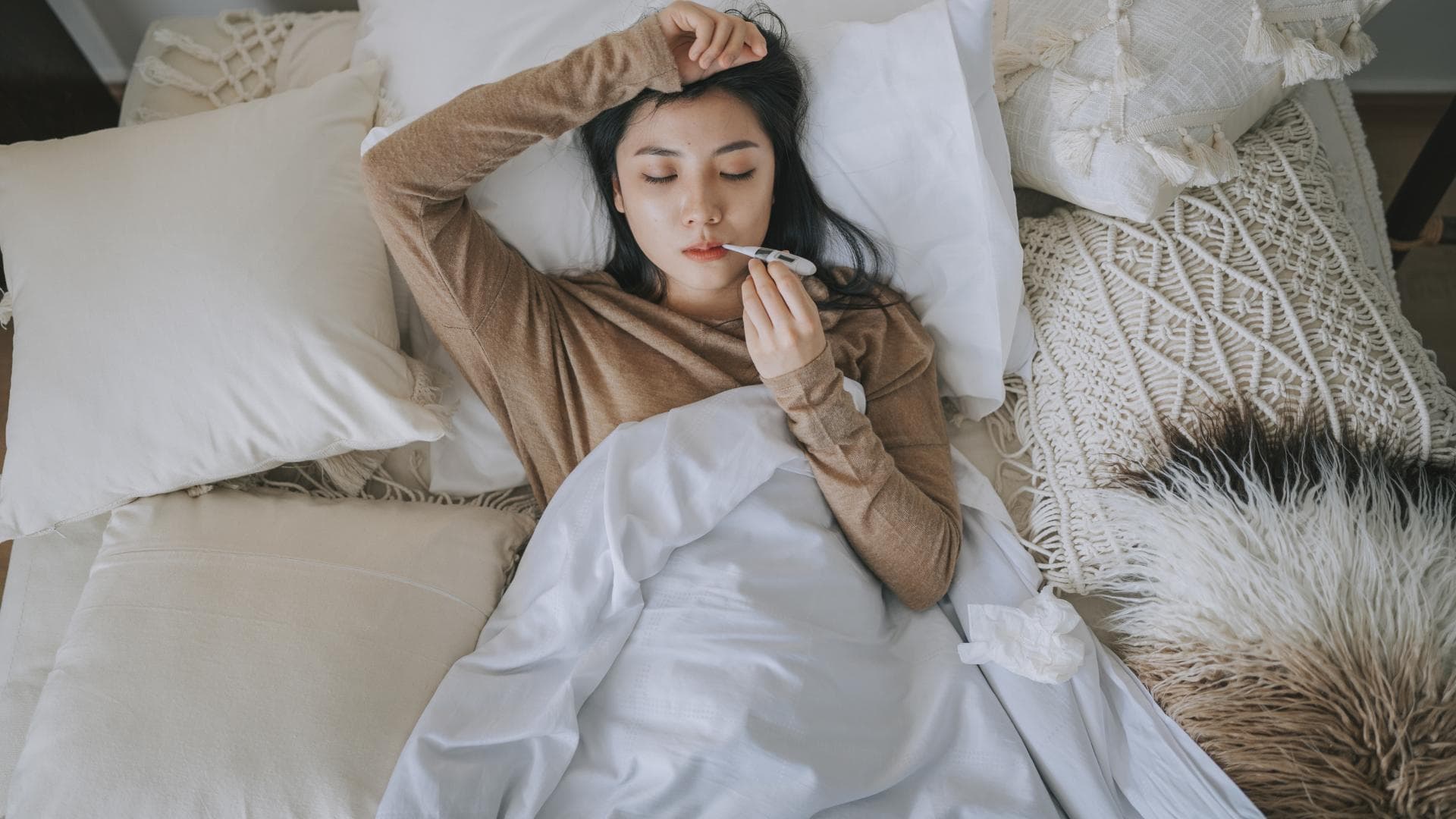 Frau liegt mit Fieberthermometer im Bett Frau liegt mit Fieberthermometer im Bett