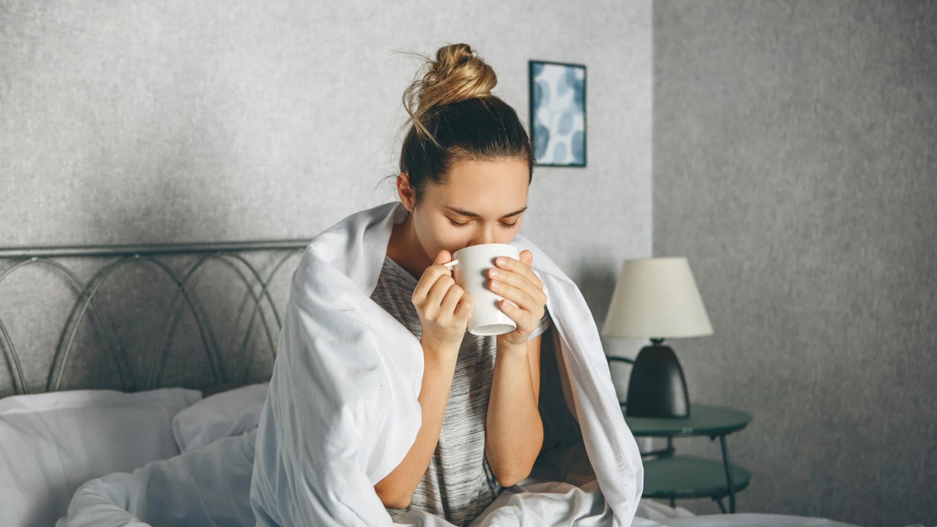 Frau sitzt im Bett und trinkt Tee