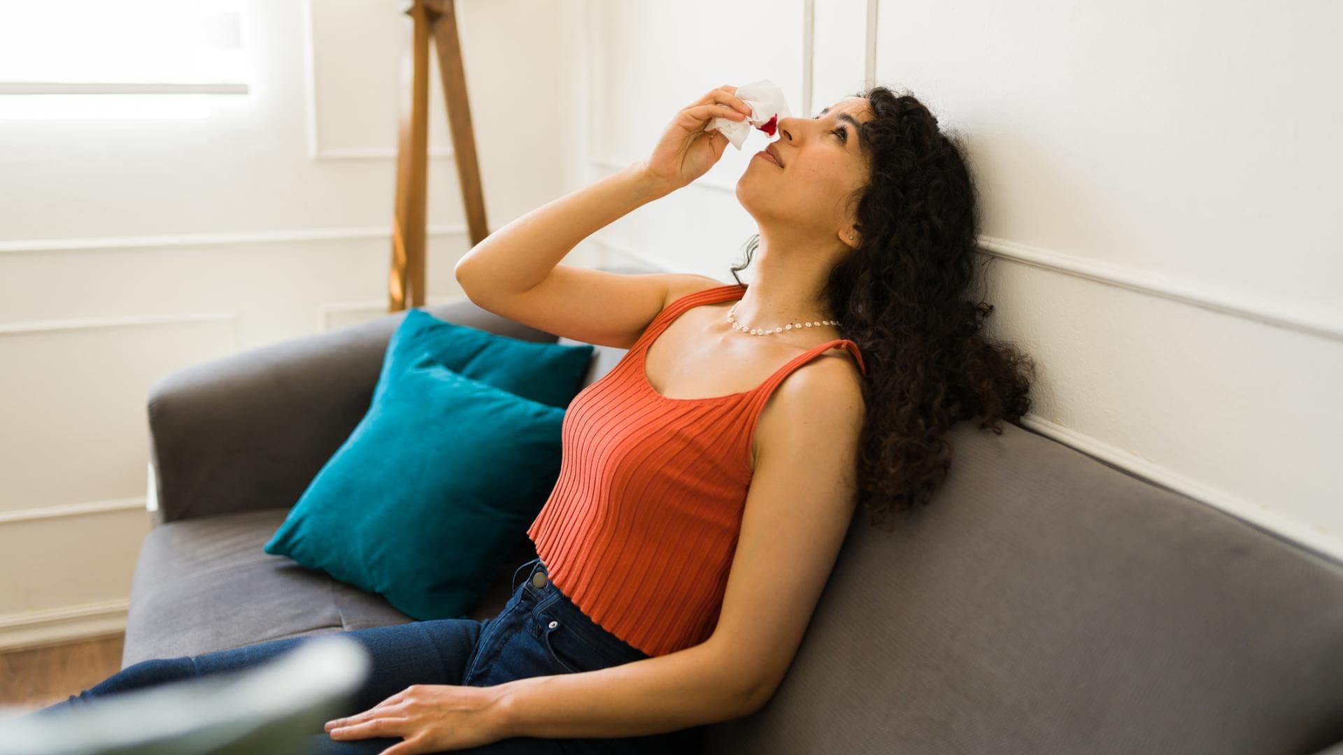 Frau sitzt auf einem Sofa und hat Nasenbluten Frau sitzt auf einem Sofa und hat Nasenbluten