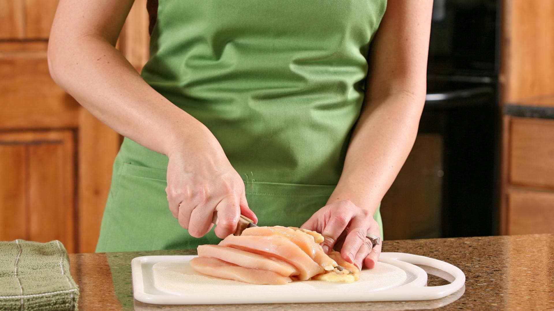 Frau schneidet rohes Hähnchen auf einem Schneidebrett Frau schneidet rohes Hähnchen auf einem Schneidebrett