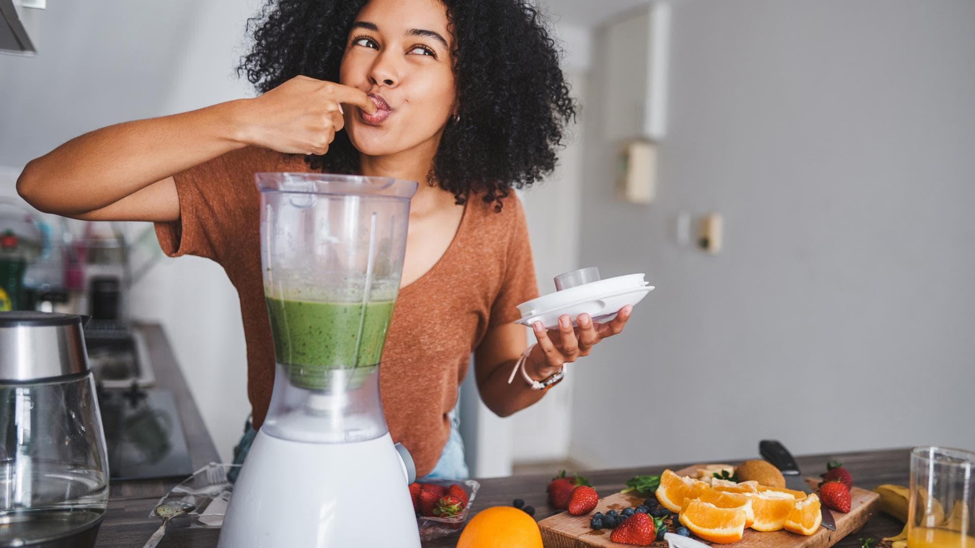 Frau steht vor dem Mixer und probiert grünen Smoothie Frau steht vor dem Mixer und probiert grünen Smoothie