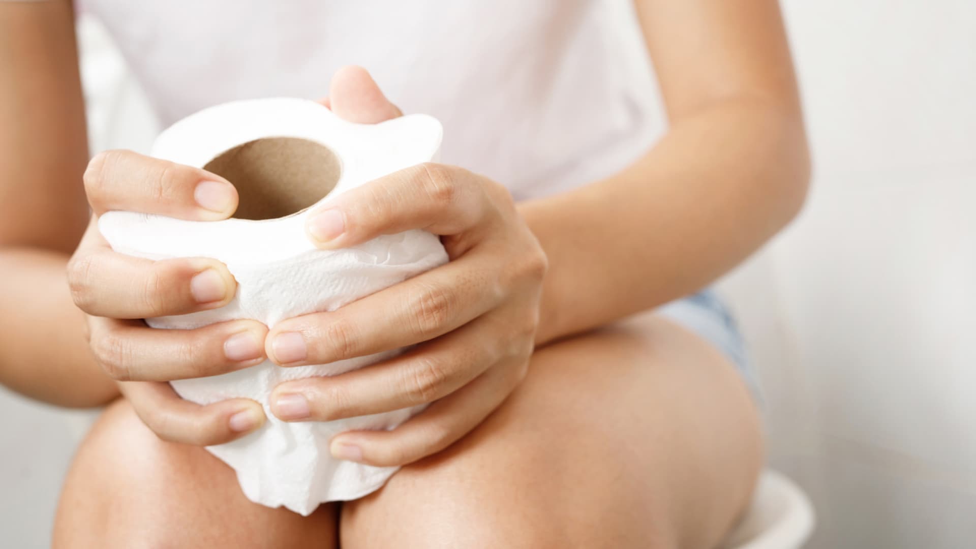 Frau sitzt auf Toilette mit einer Rolle Toilettenpapier in der Hand Frau sitzt auf Toilette mit einer Rolle Toilettenpapier in der Hand