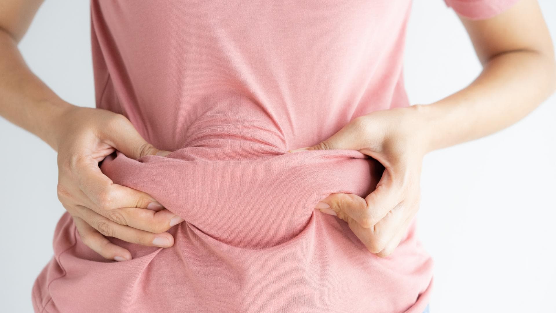 Frau fasst das Fett am Bauch unter ihrem T-Shirt an Frau fasst das Fett am Bauch unter ihrem T-Shirt an