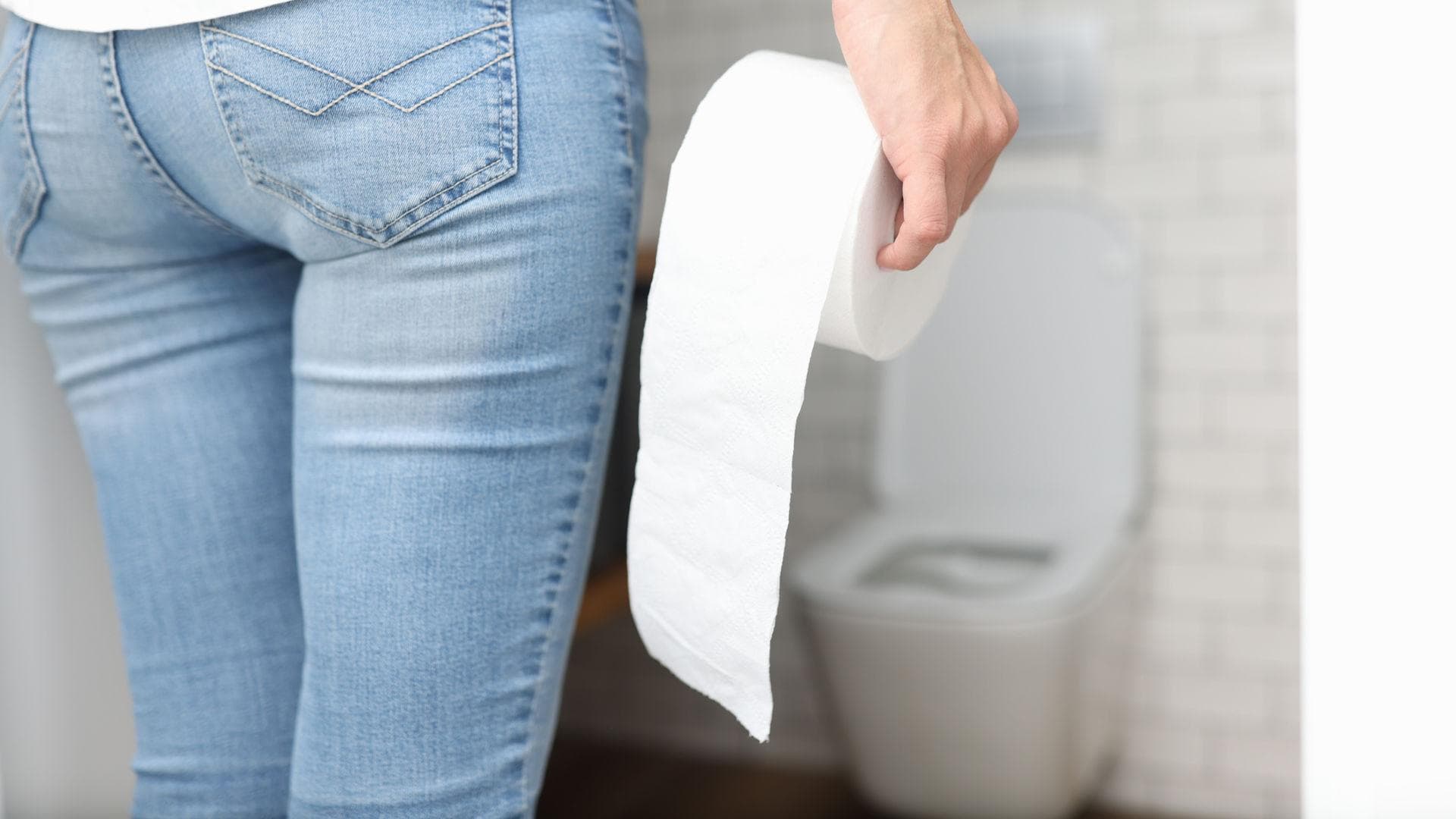 Frau steht vor der Toilette und hält eine Rolle Toilettenpapier in der Hand Frau steht vor der Toilette und hält eine Rolle Toilettenpapier in der Hand