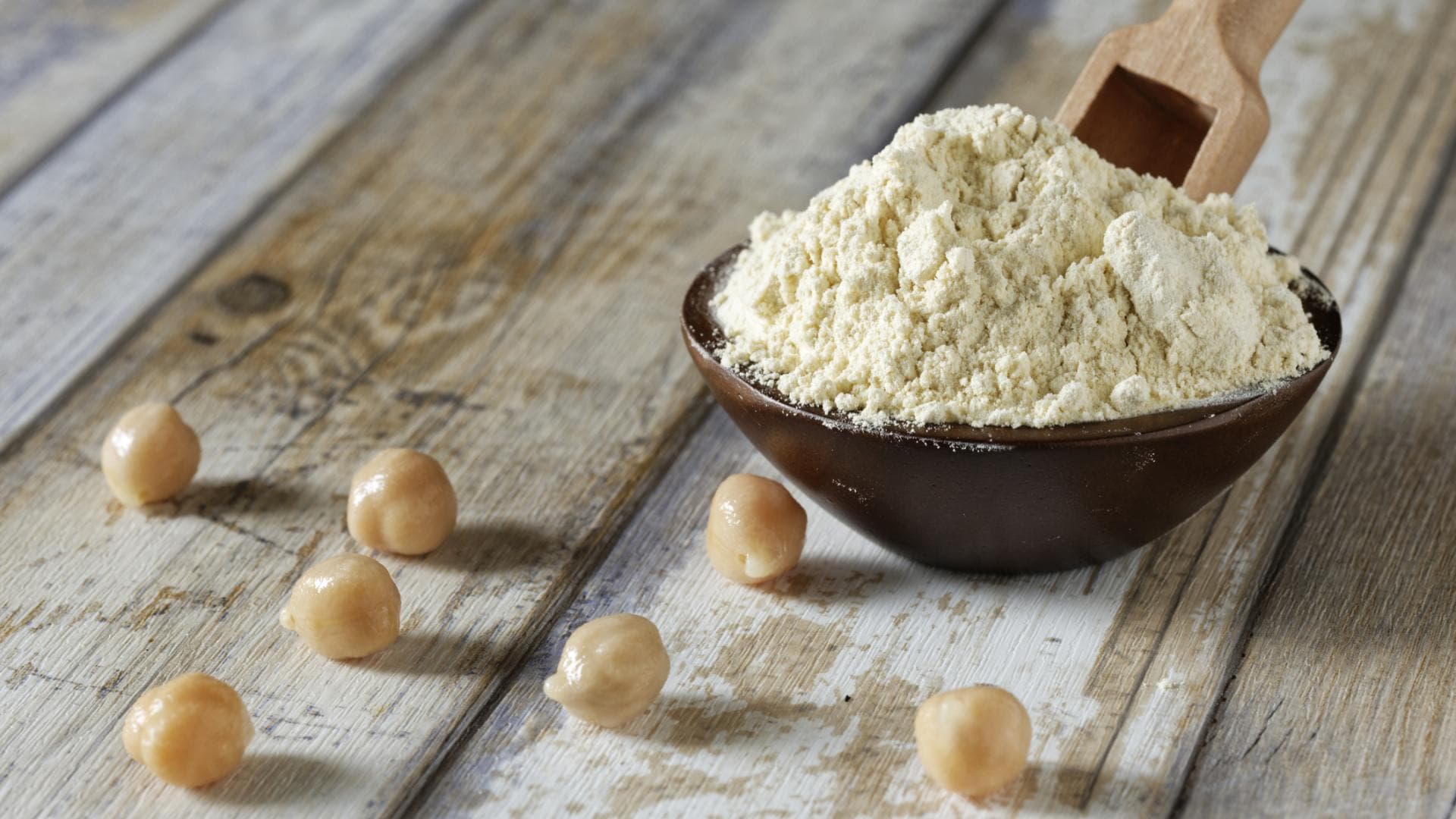 Kichererbsenmehl neben vereinzelten Kichererbsen Löffel mit Kichererbsenmehl neben vereinzelten Kichererbsen