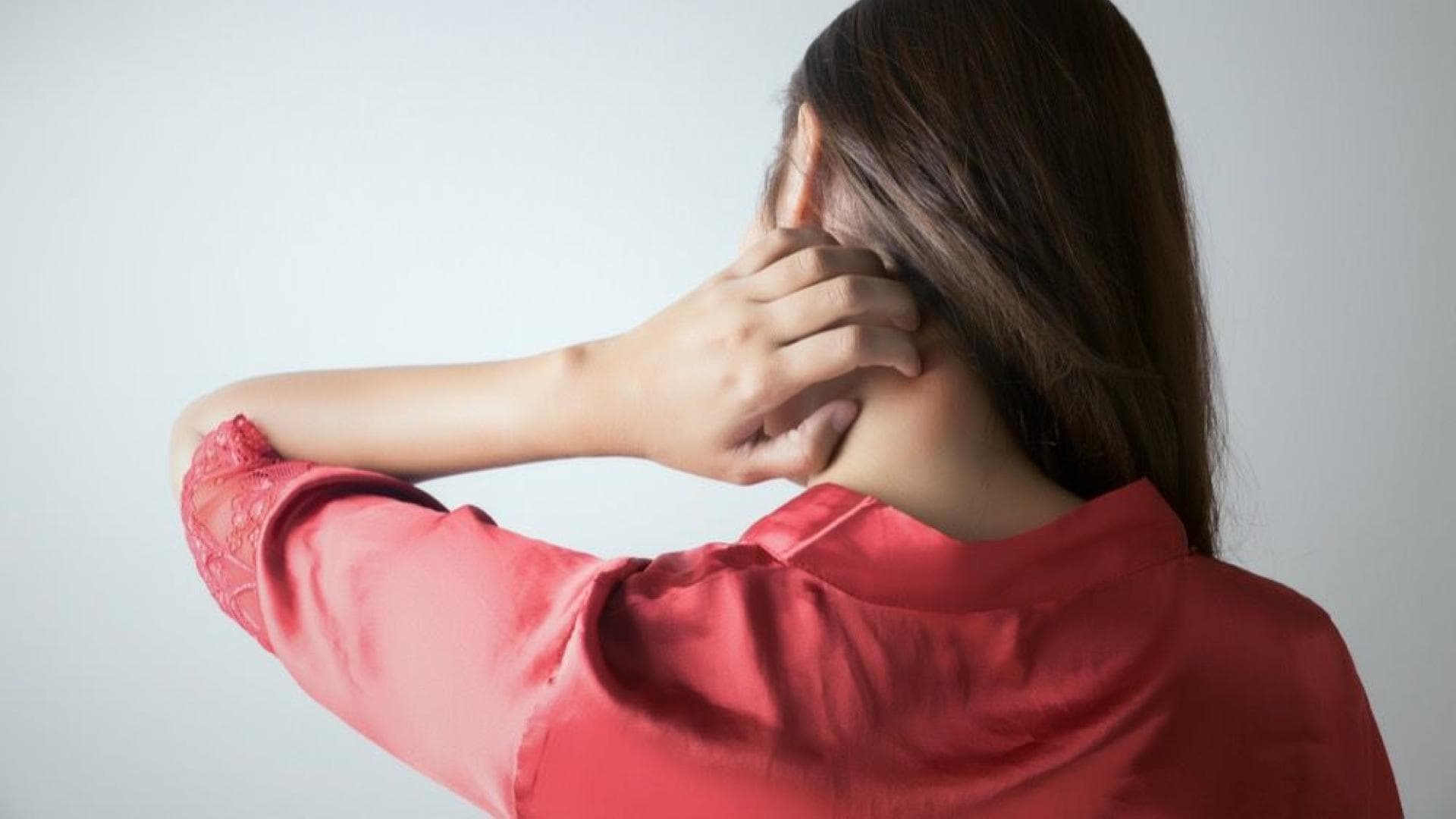 Frau juckt sich mit der Hand am Nacken.