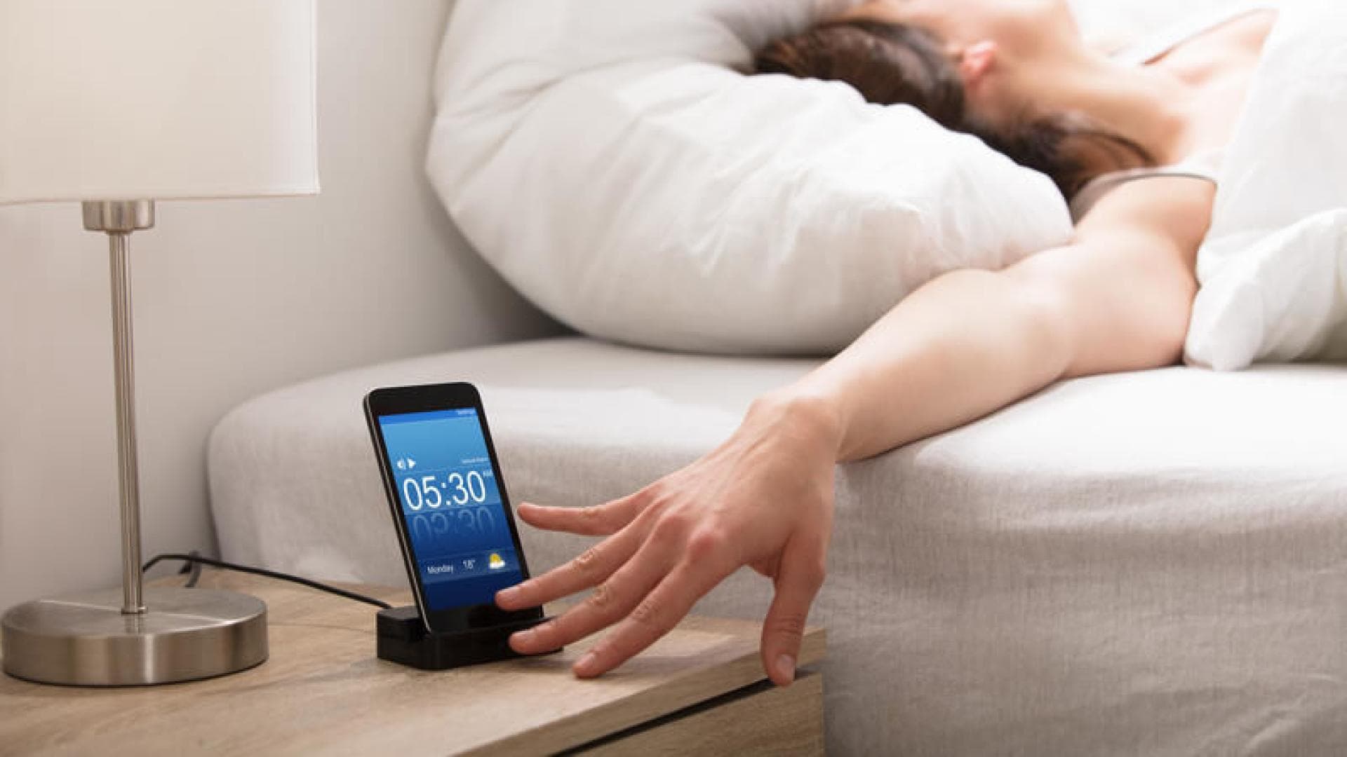 Wecker_Schlafen Frau im Bett drückt Snooze Taste Wecker