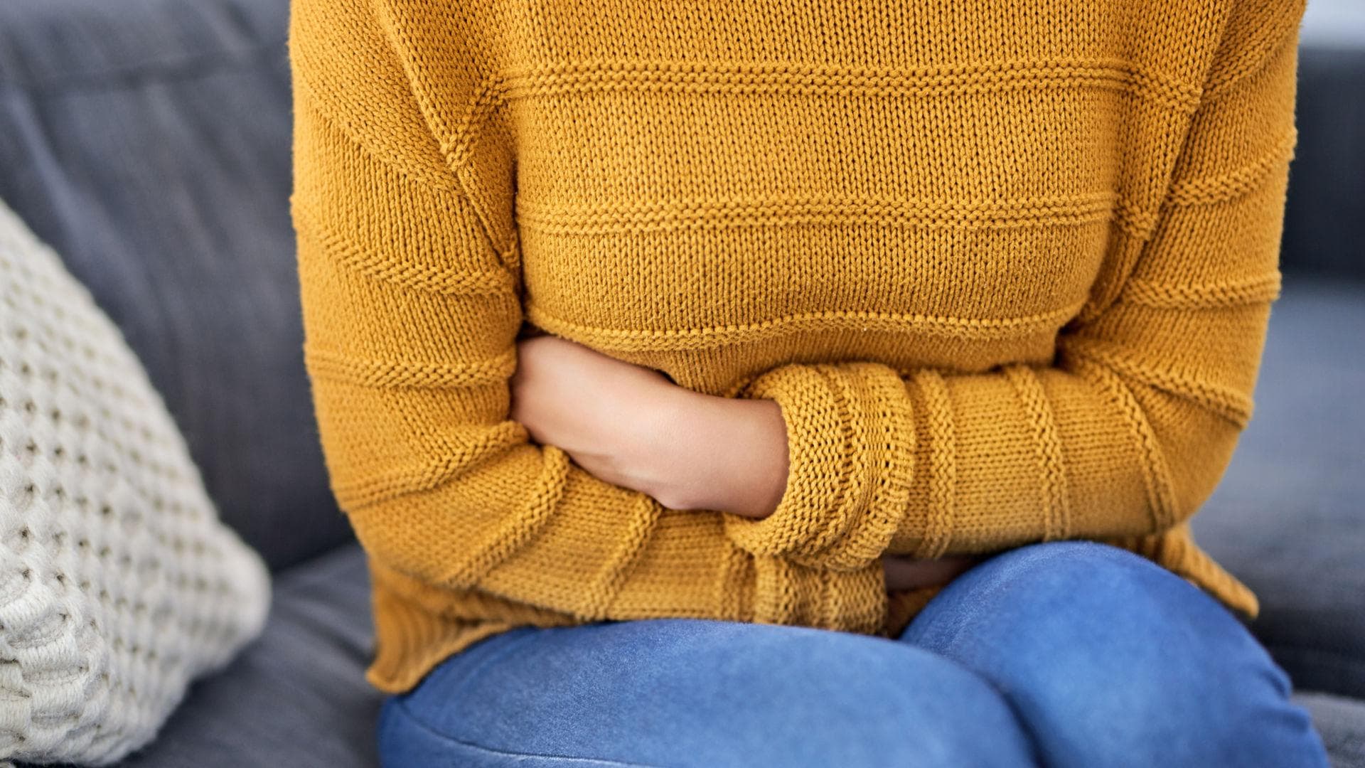 Frau sitzt auf Sofa und hält sich den Bauch