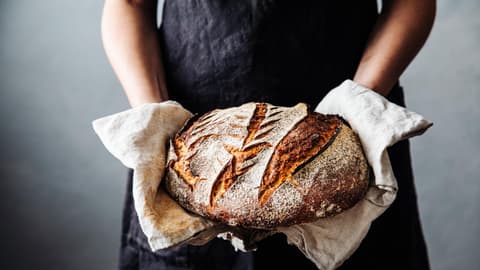 Bäckerin hält frisches Sauerteigbrot in den Händen
