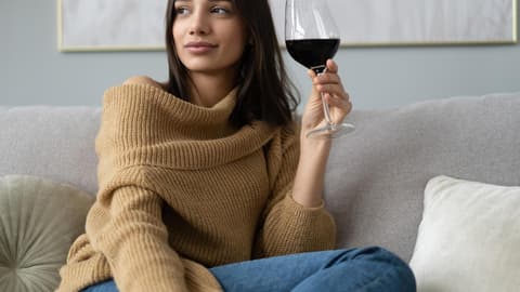 Frau sitzt mit einem Glas Rotwein auf dem Sofa