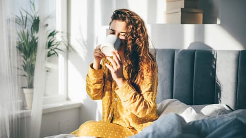 Frau trinkt im Bett eine Tasse Kaffee