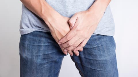 Mann hält sich Hand vor dem Intimbereich