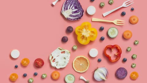 Gemüse wie Paprika, Kohl, Blumenkohl, Paprika und mehr halbiert und dekorativ auf rosafarbenem Hintergrund drapiert