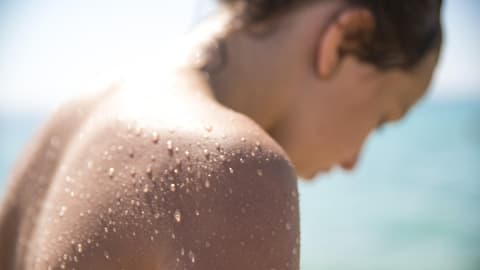 Eine Junge Frau, die sich im Sommer am Wasser befindet und deren Rücken mit Wasserperlen überzogen ist