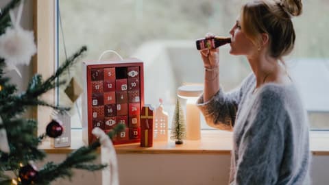 Eine junge Frau hat das erste Türchen ihres Rabenhorst-Adventskalenders geöffnet und trinkt einen Schluck aus der Mini-Saftflasche 