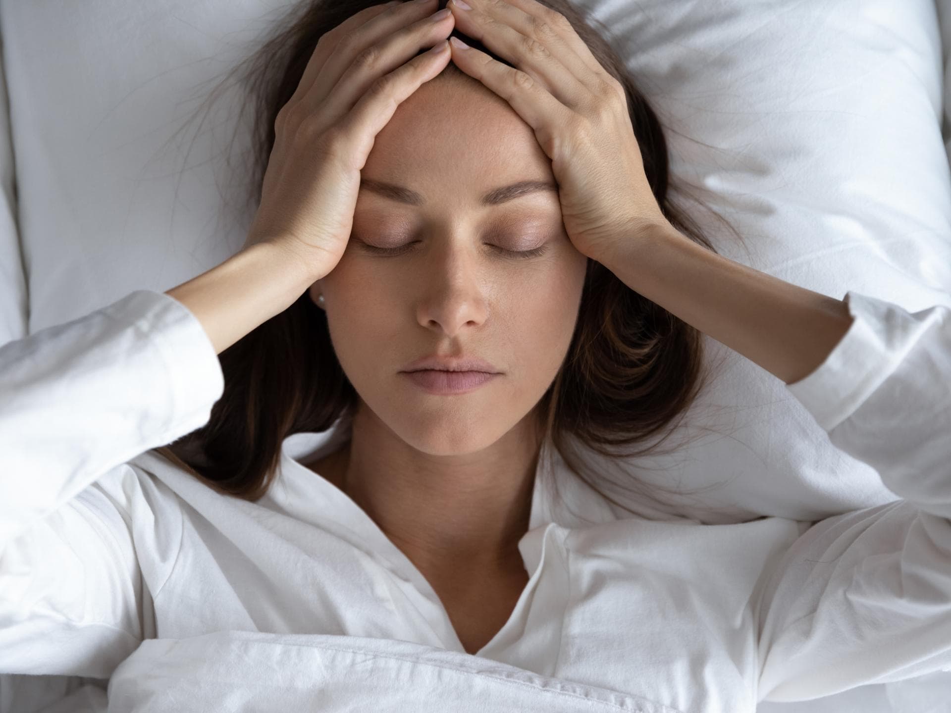 Frau liegt im Bett und hält sich den Kopf