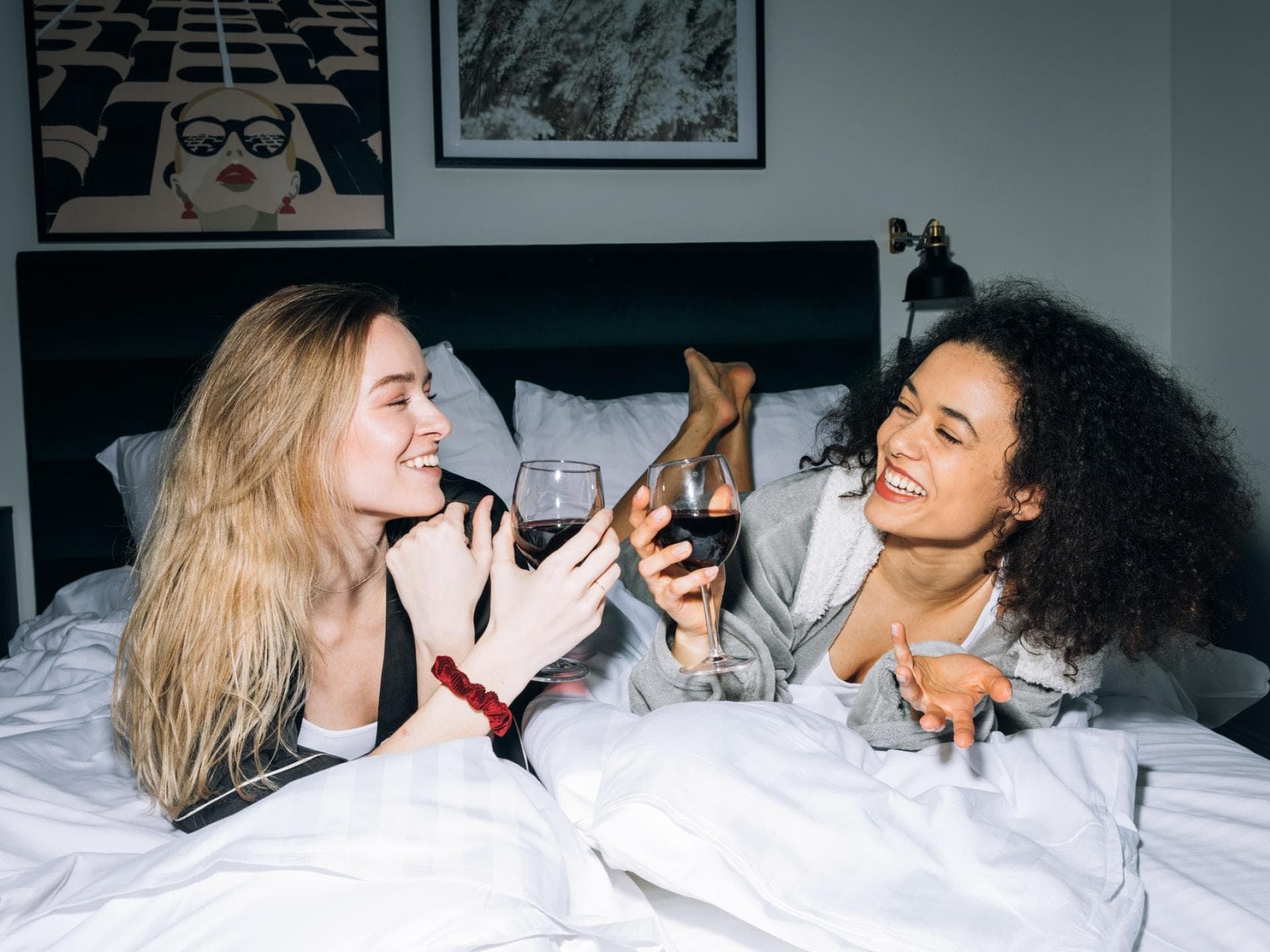 Frauen liegen auf einem Bett und trinken Rotwein