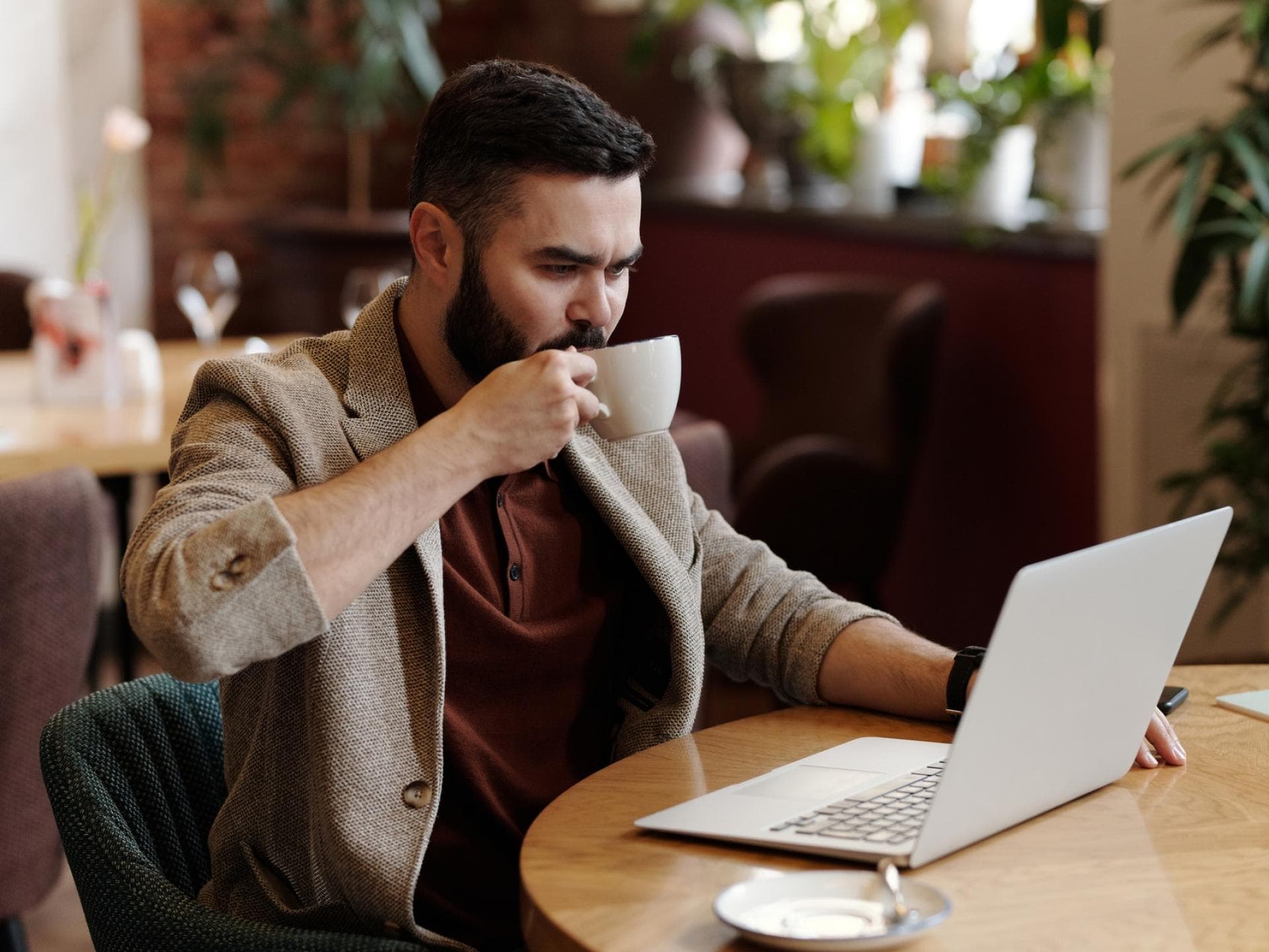 Mann sitzt vor einem Laptop und trinkt Kaffee