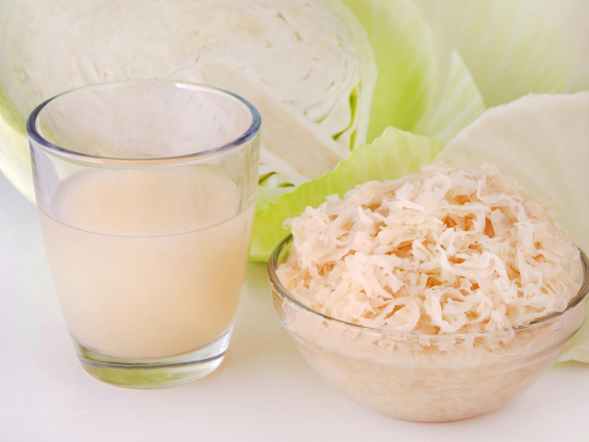 Sauerkraut und Sauerkrautsaft vor aufgeschnittenem Weißkohl
