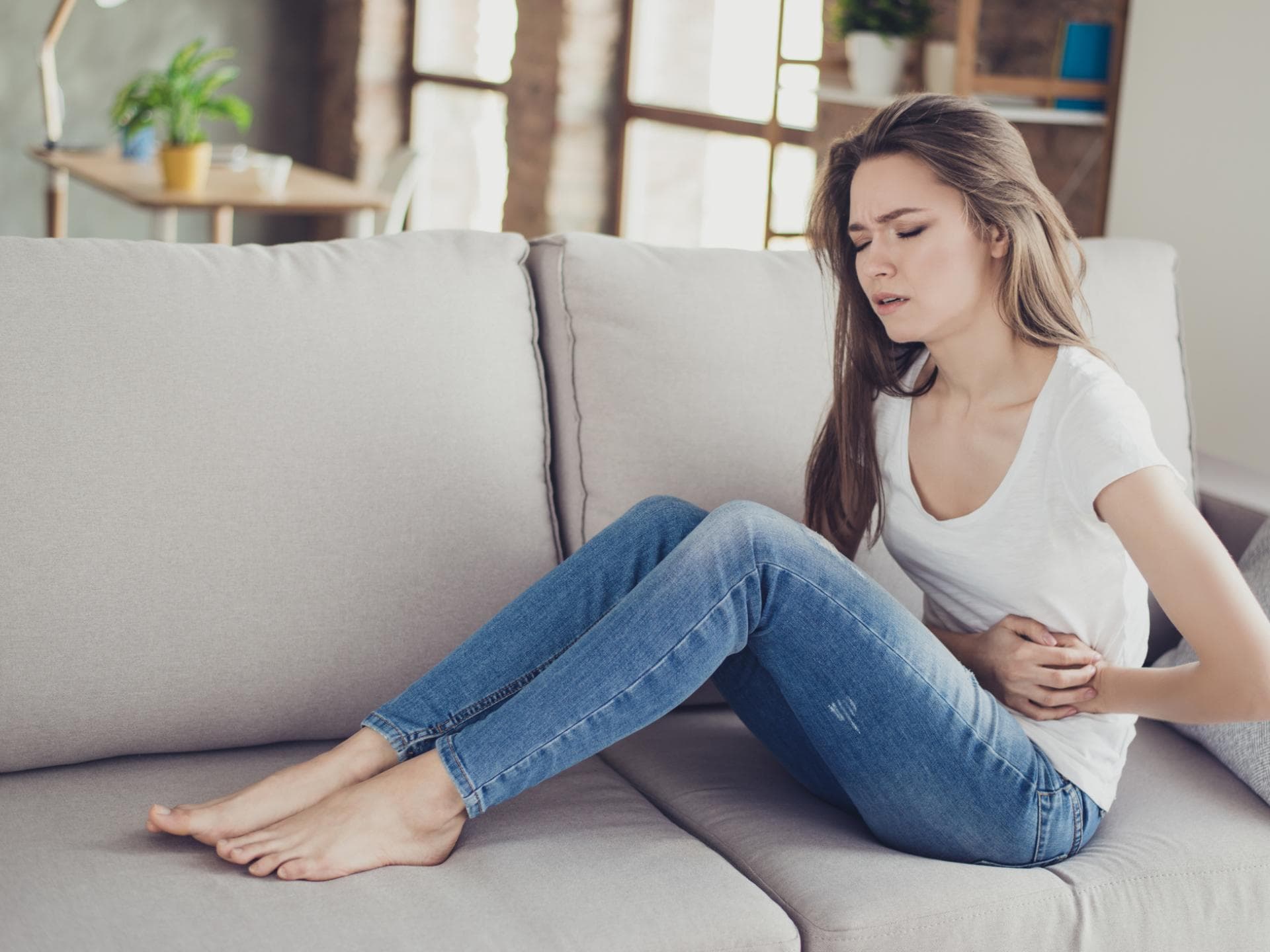 Frau mit Bauchschmerzen sitzt auf Couch