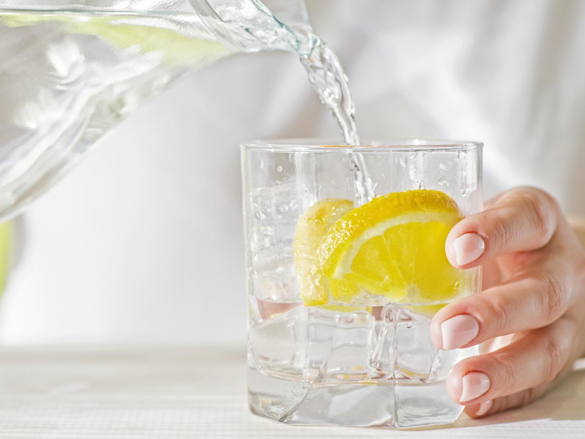 Wasser wird in ein Glas mit Zitrone gegossen