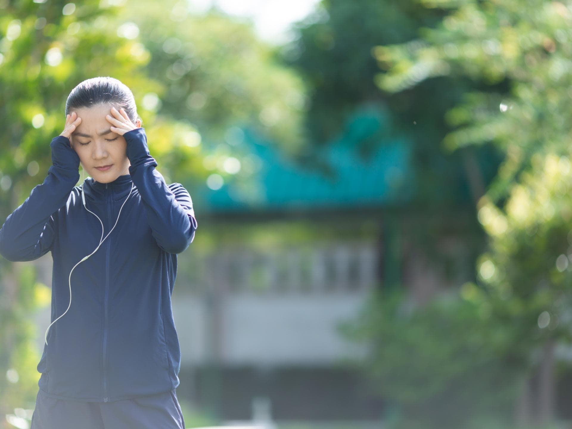 Joggerin mit Erkältung fasst sich an schmerzenden Kopf