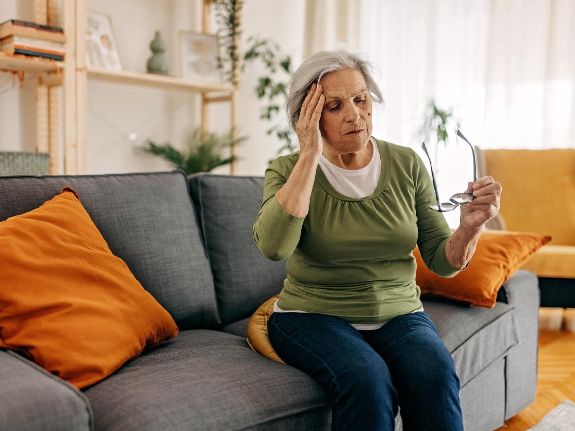Alte Frau auf der Couch fasst sich wegen Schwindel an den Kopf