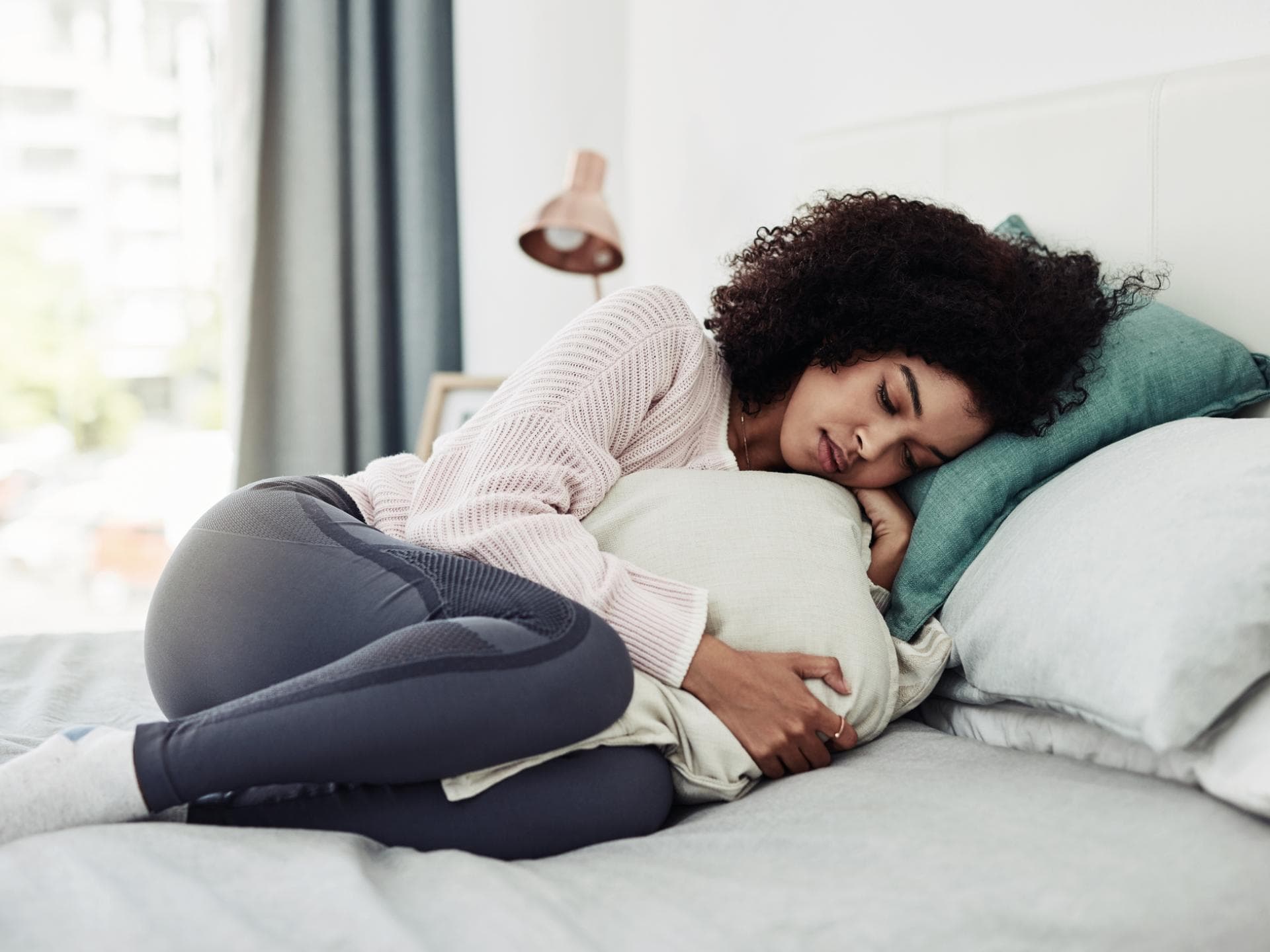Frau liegt mit Bauchschmerzen im Bett