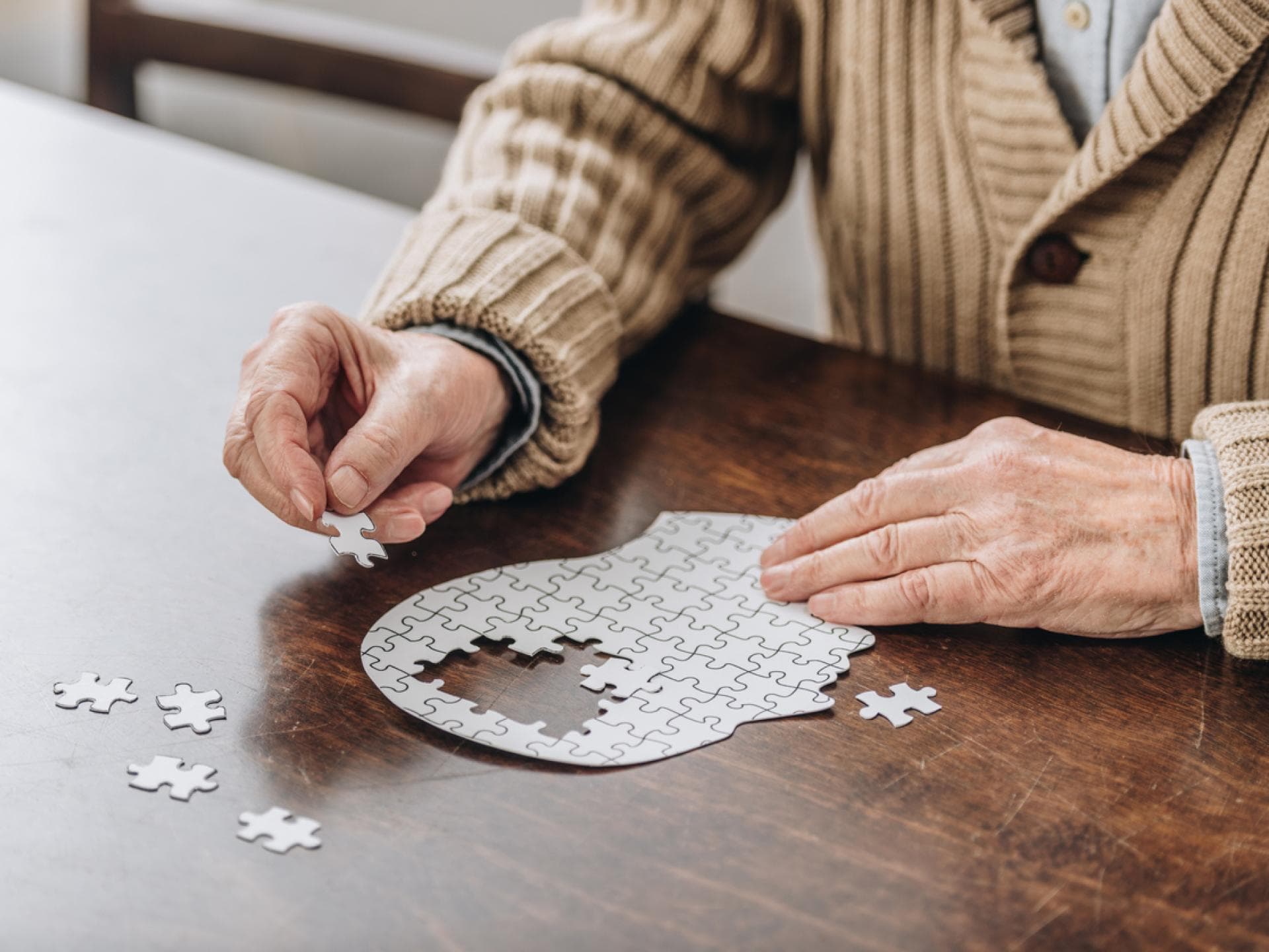Alzheimer ist durch den Verlust von Nervenzellen im Gehirn gekennzeichnet. Alter Mann puzzelt auf Tisch